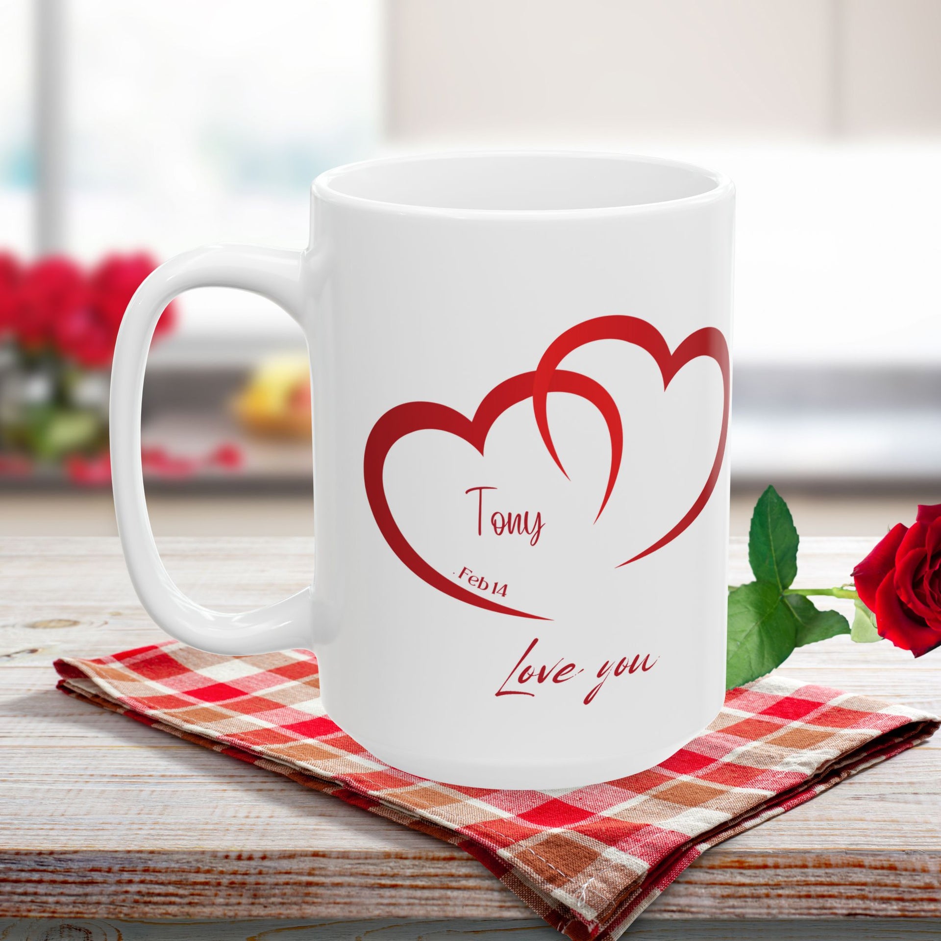 A white ceramic mug with two red heart shapes and the words 'Love you' printed on one side, placed on a wooden surface with a plant in the background.