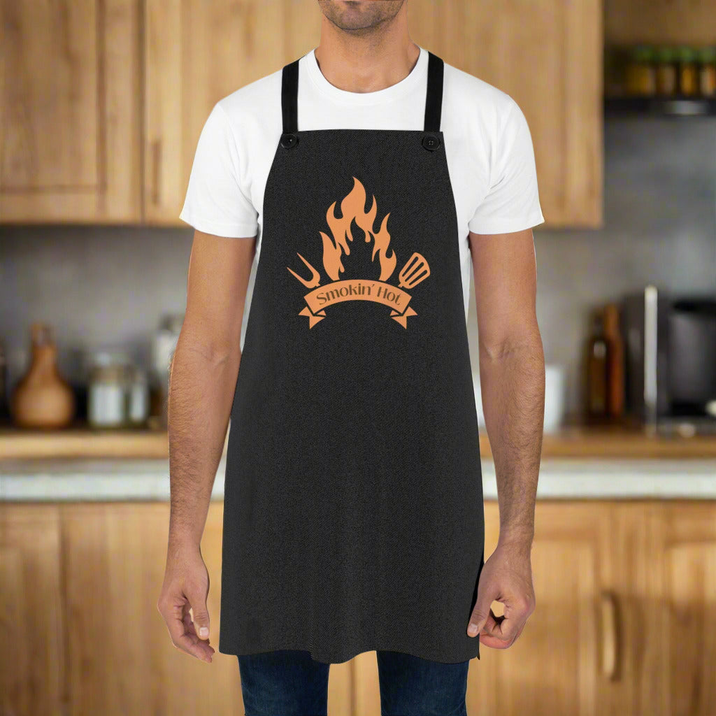 A person wearing a black apron with a 'SMOKING HOT' text and flame design on the front.