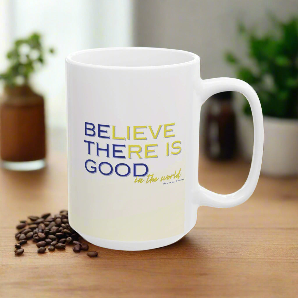 A white ceramic coffee mug with blue and yellow text that reads 'BELIEVE THERE IS GOOD in the world'.
