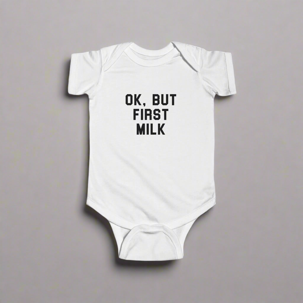 White baby one piece that has black text saying "Ok, but first milk"