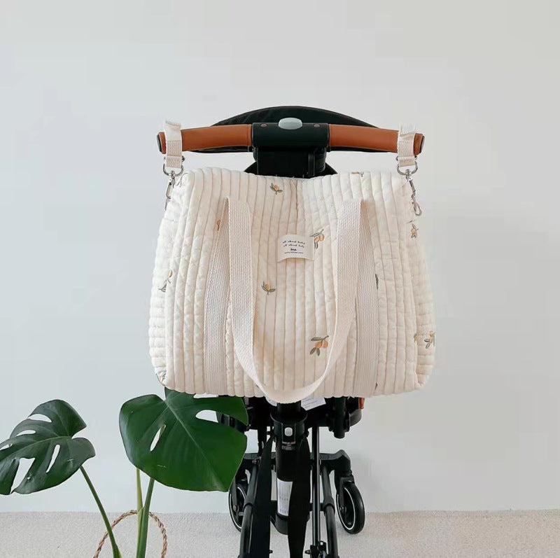 White textured diaper bag on a black stroller against a white wall.