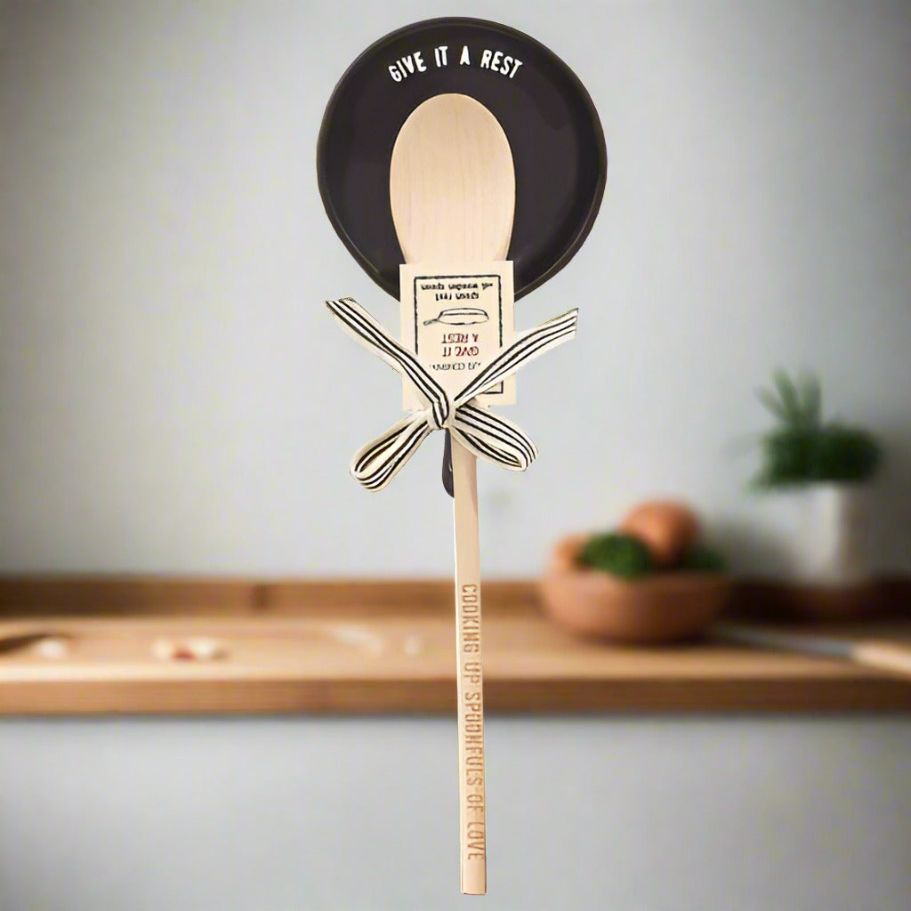Wooden spoon with engraved handle reading “Cooking Up Something to Love,” paired with black ceramic spoon rest labeled “Give It a Rest,” tied with decorative striped bow, unique kitchen gift set for cooking and home décor.