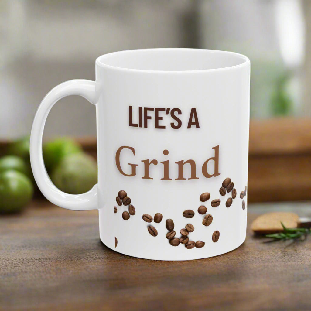 A white ceramic mug with 'LIFE'S A Grind' text and coffee beans scattered around the bottom.