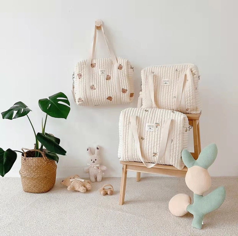 Textured diaper bags and cushions on a wooden stool with toys and a plant in a minimalistic setting
