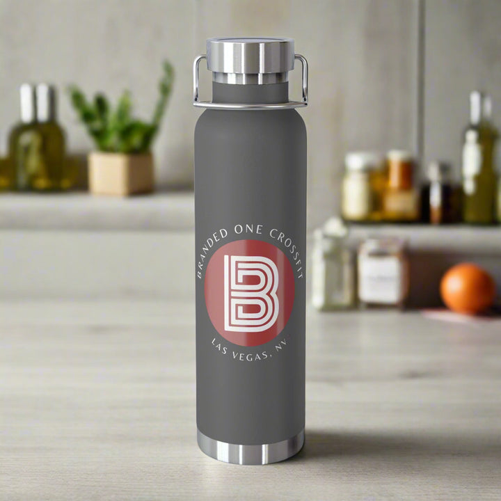 A dark gray copper vacuum insulated bottle with a white and red Branded one Crossfit logo