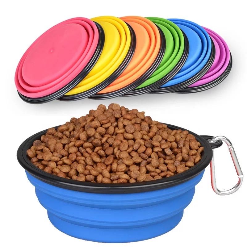 A collection of collapsible silicone pet bowls in various colors displayed both expanded and folded, with one bowl filled with pet food and a carabiner attached.