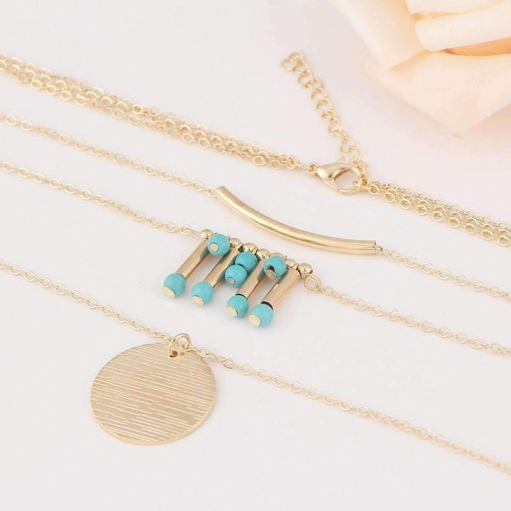 A three-layered gold-tone necklace with turquoise beads and a gold coin pendant on a white background.