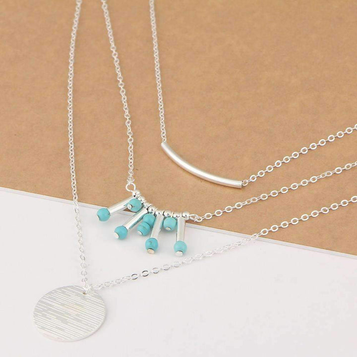 A three-layered silver-tone necklace with turquoise beads and a gold coin pendant on a white background.