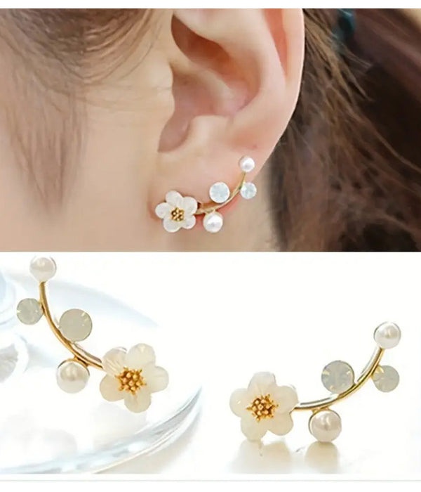A pair of gold-colored earrings featuring a resin flower design with pearl accents, displayed on a woman's ear and on a table.