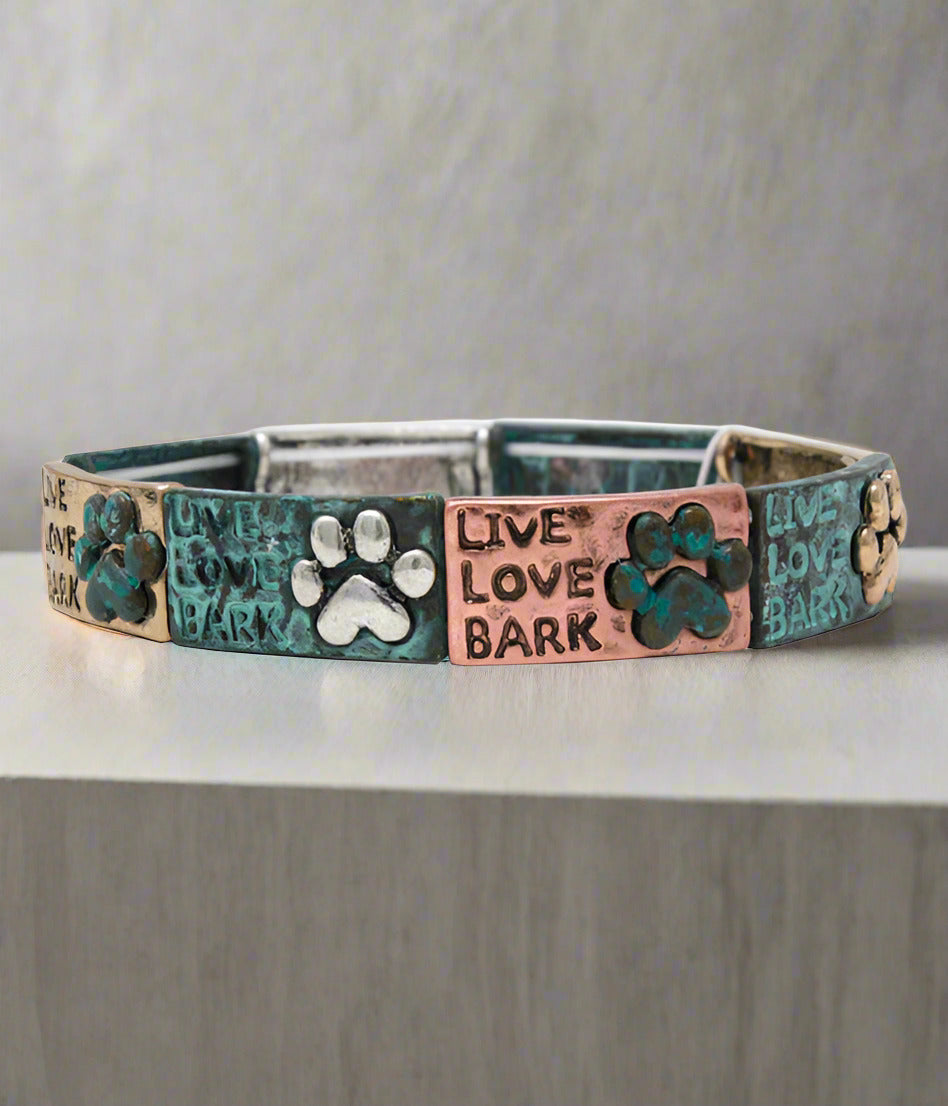A multicolored stretch bracelet with metallic and leather accents, featuring text and paw print designs.