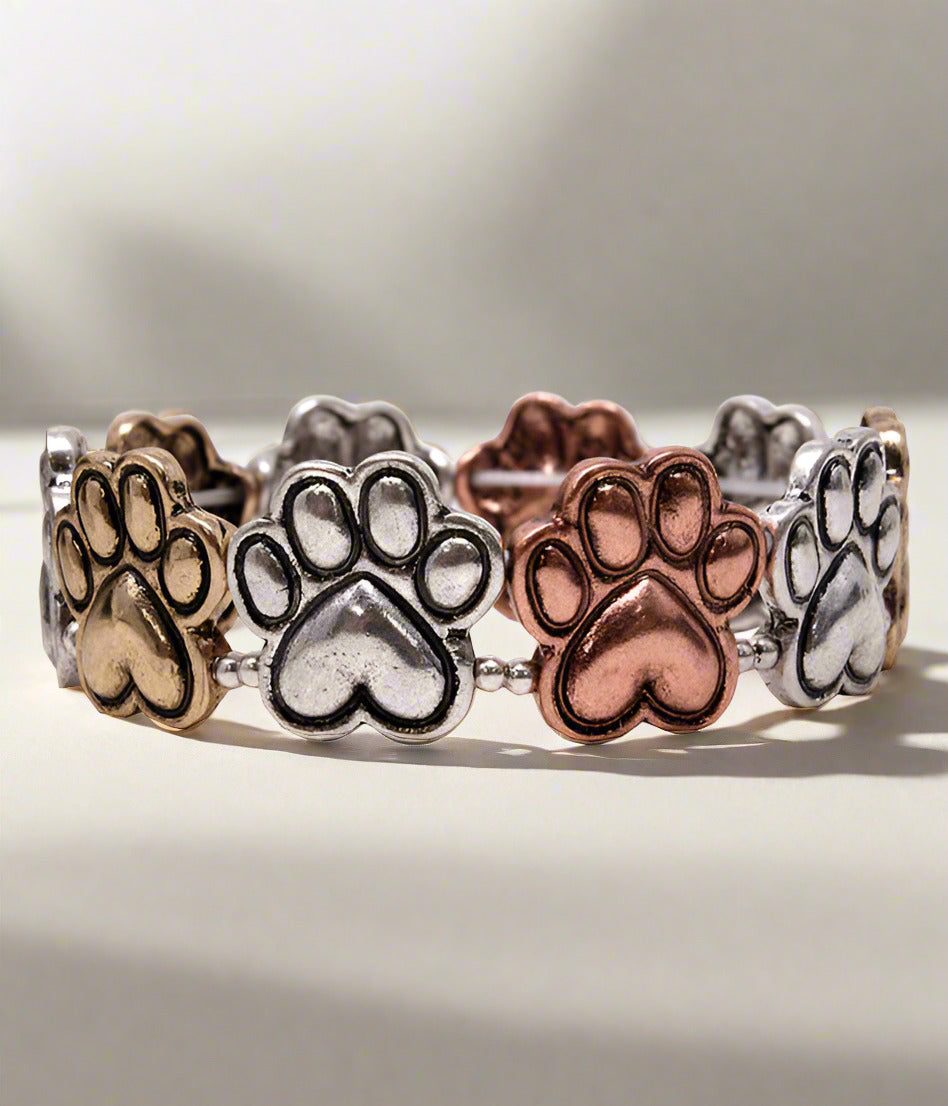 A stretch bracelet featuring metallic paw prints in gold, silver, and rose gold colors.