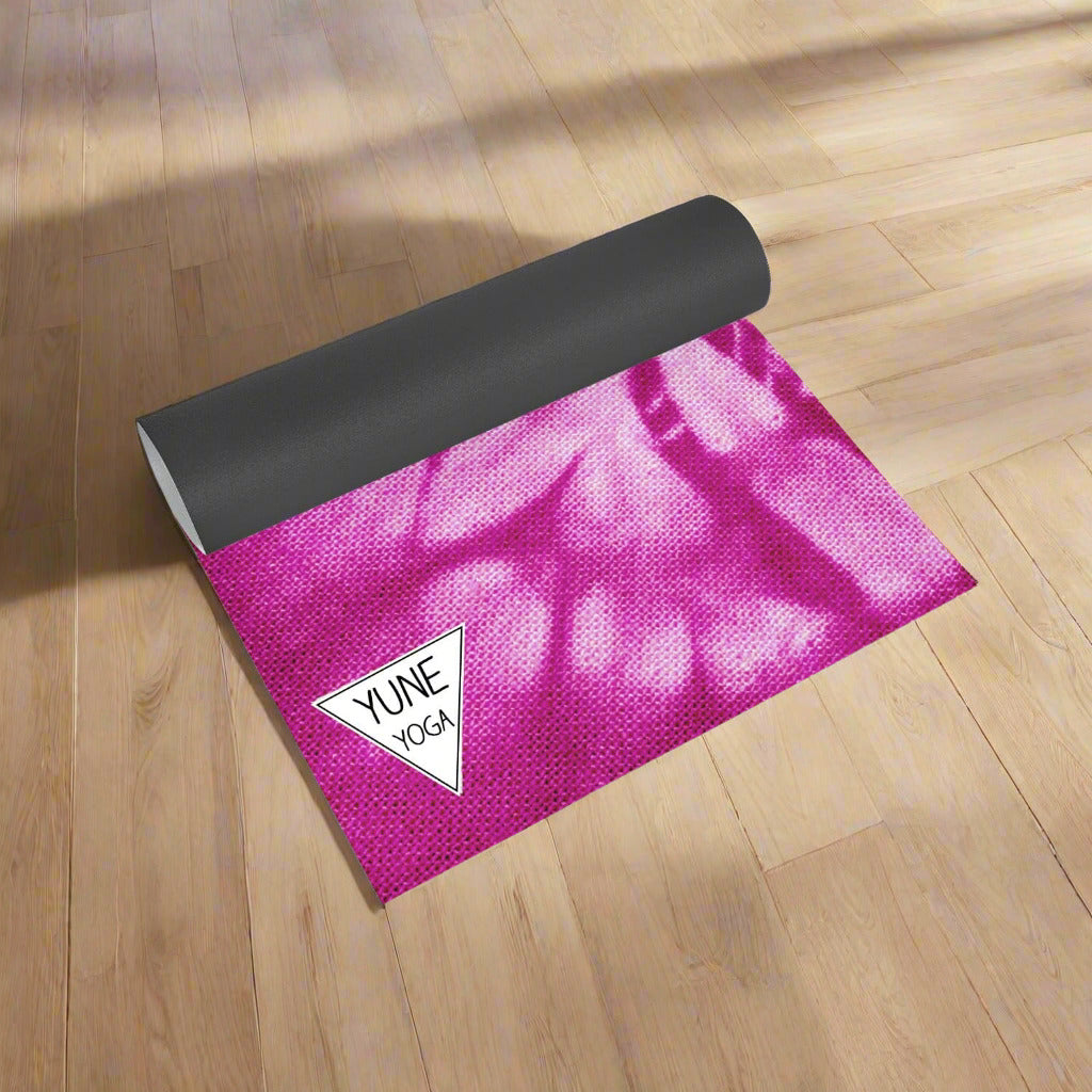 Pink tie-dye yoga mat with black edge on a wooden floor