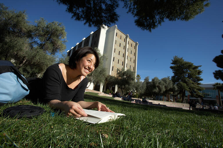 Student enjoying reading in the grass, supporting UNLV College of Liberal Arts in a sunny outdoor setting.
