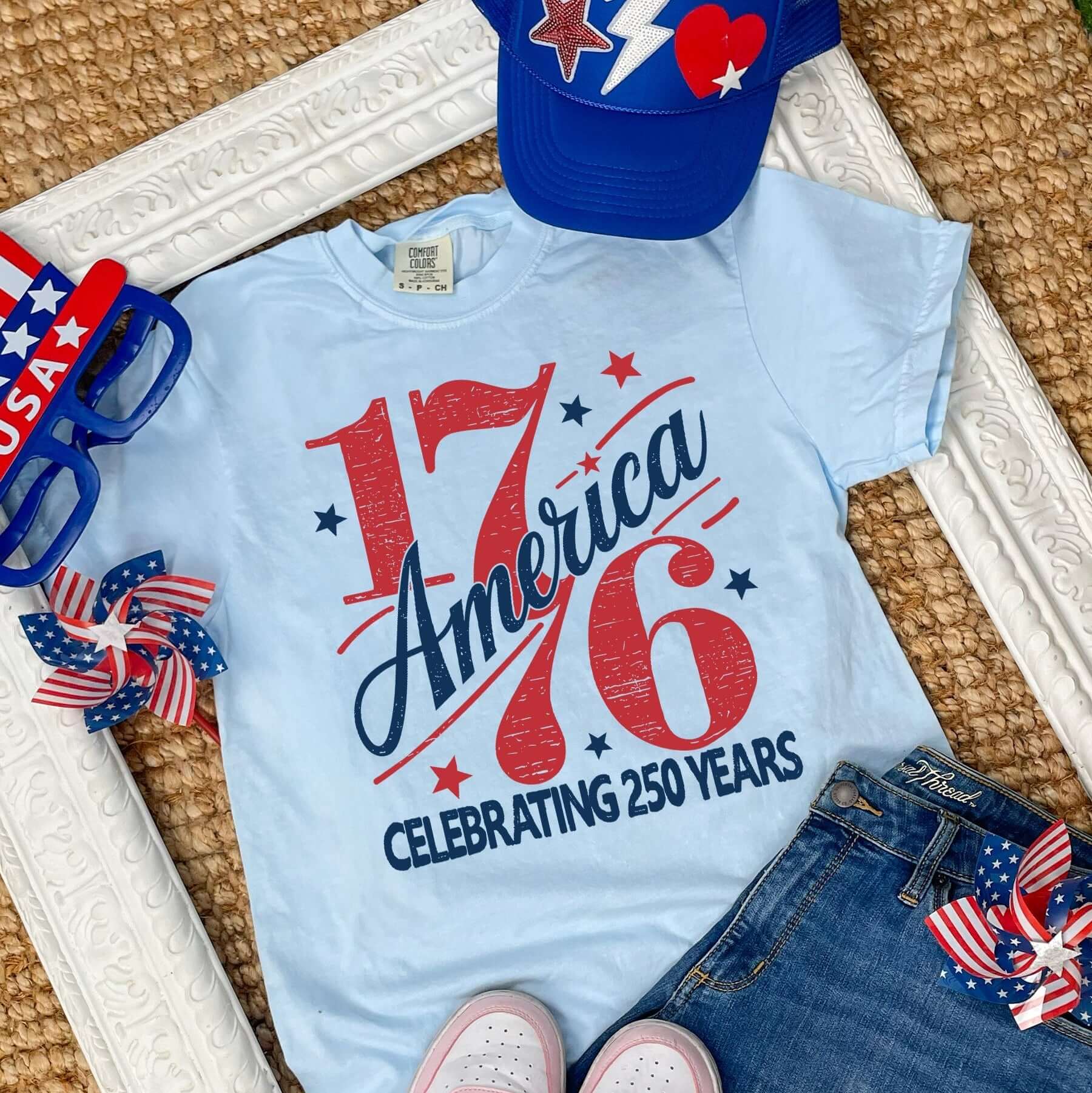 1776 America patriotic Comfort Colors graphic t shirt laid flat with denim shorts patriotic accessories and USA themed styling