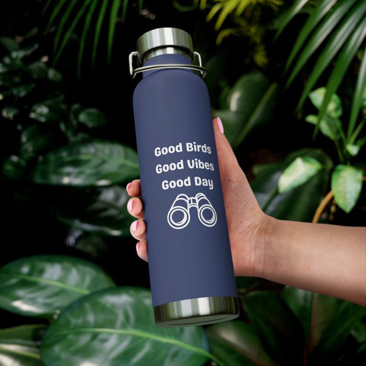 Birding copper vacuum insulated water bottle 22oz with bird binocular design in hand surrounded by green foliage