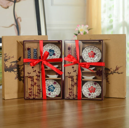Two sets of decorative plates with floral designs in a cardboard box with red ribbons.