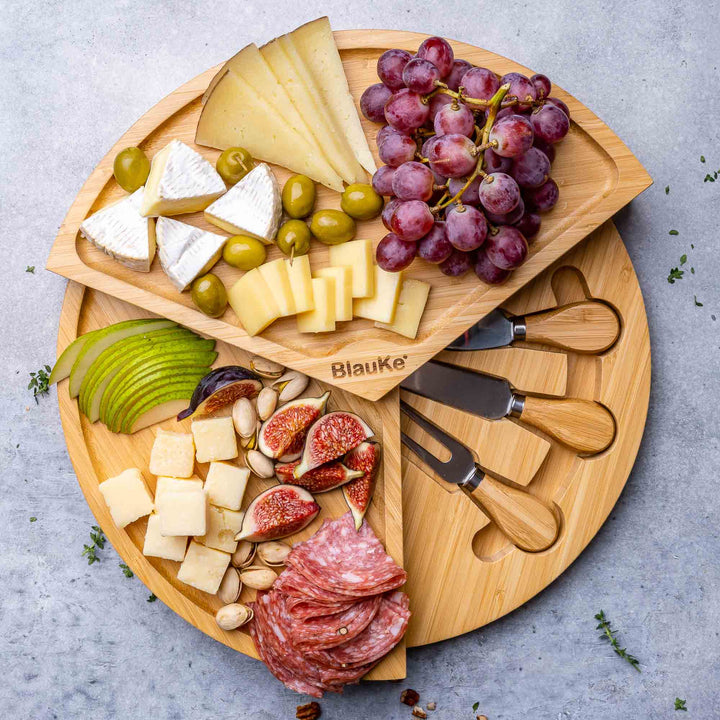 Wooden charcuterie board with cheeses, fruits, and meats, featuring Blauke branding.