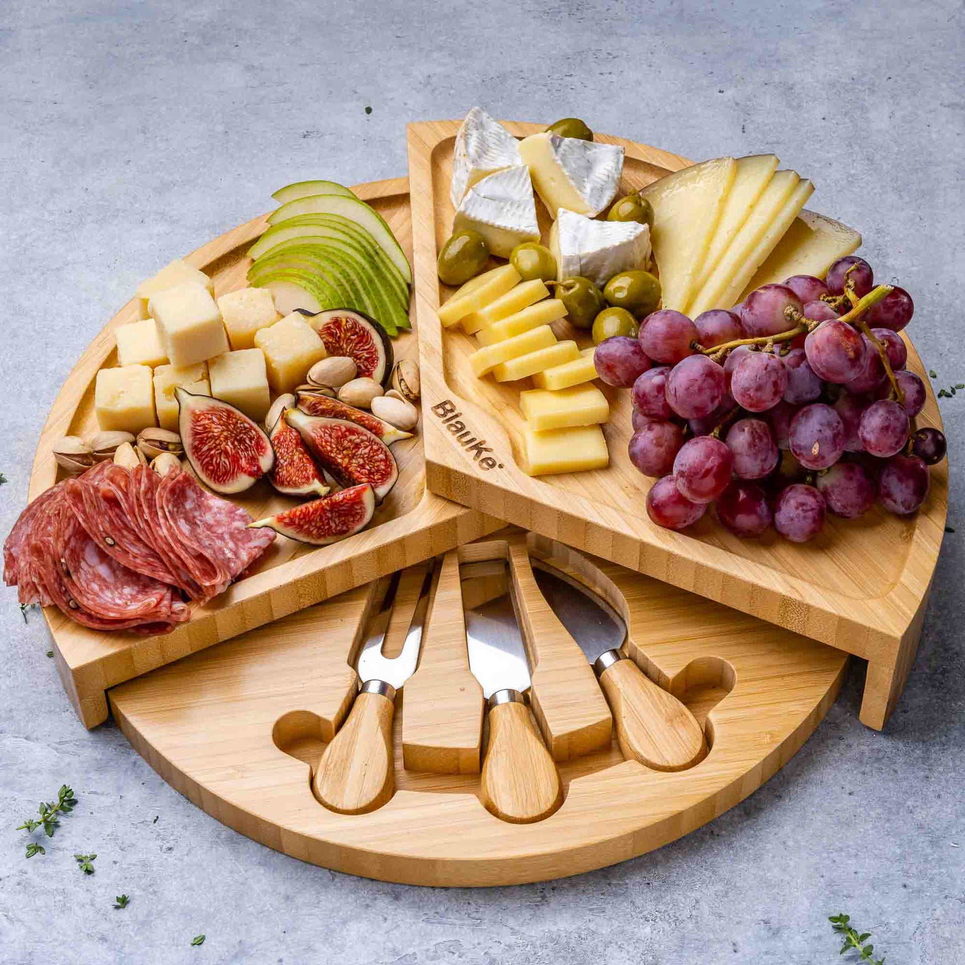 Wooden charcuterie board with assorted meats, cheeses, and fruits on a gray surface.