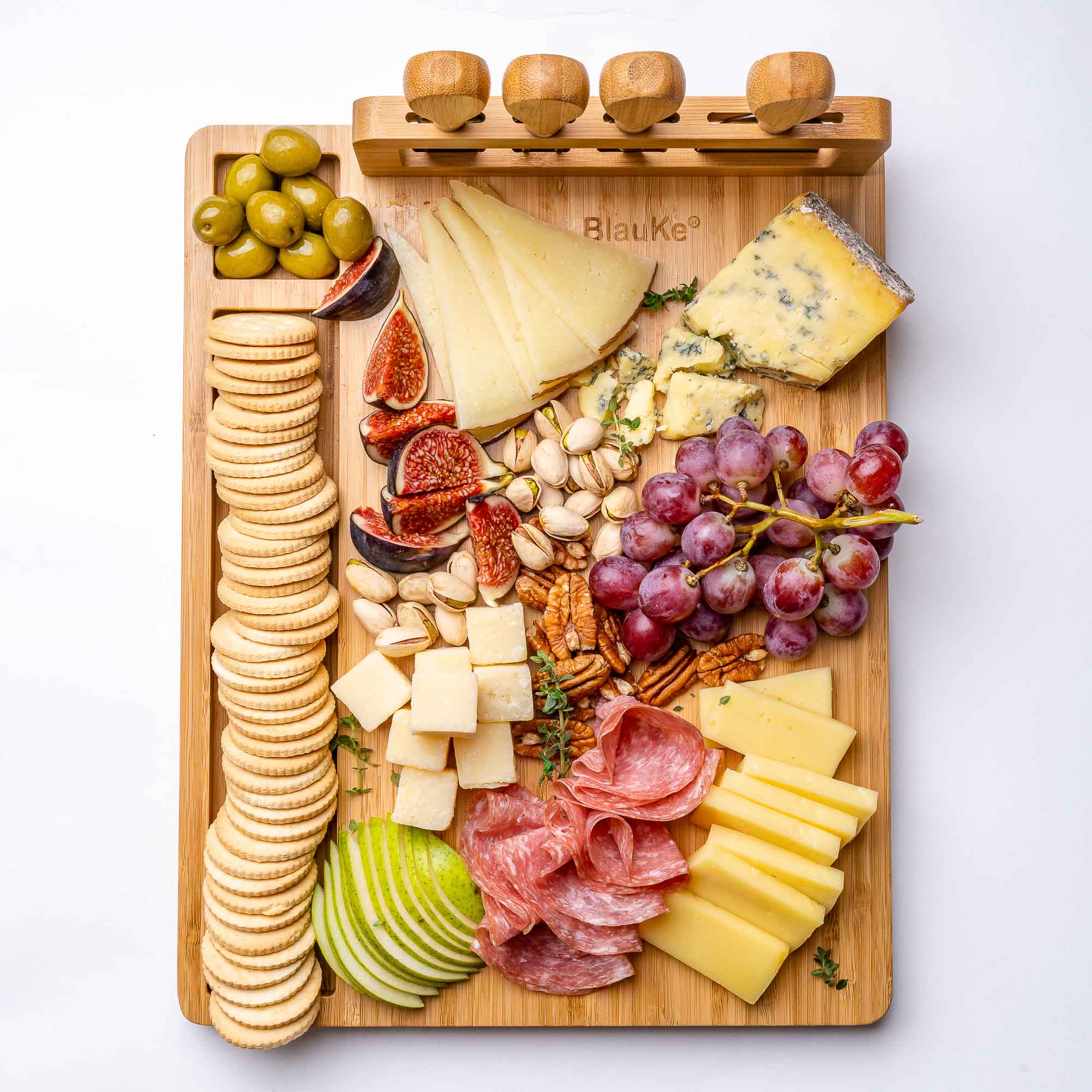 Wooden charcuterie board with various cheeses, meats, fruits, and crackers on a white background.