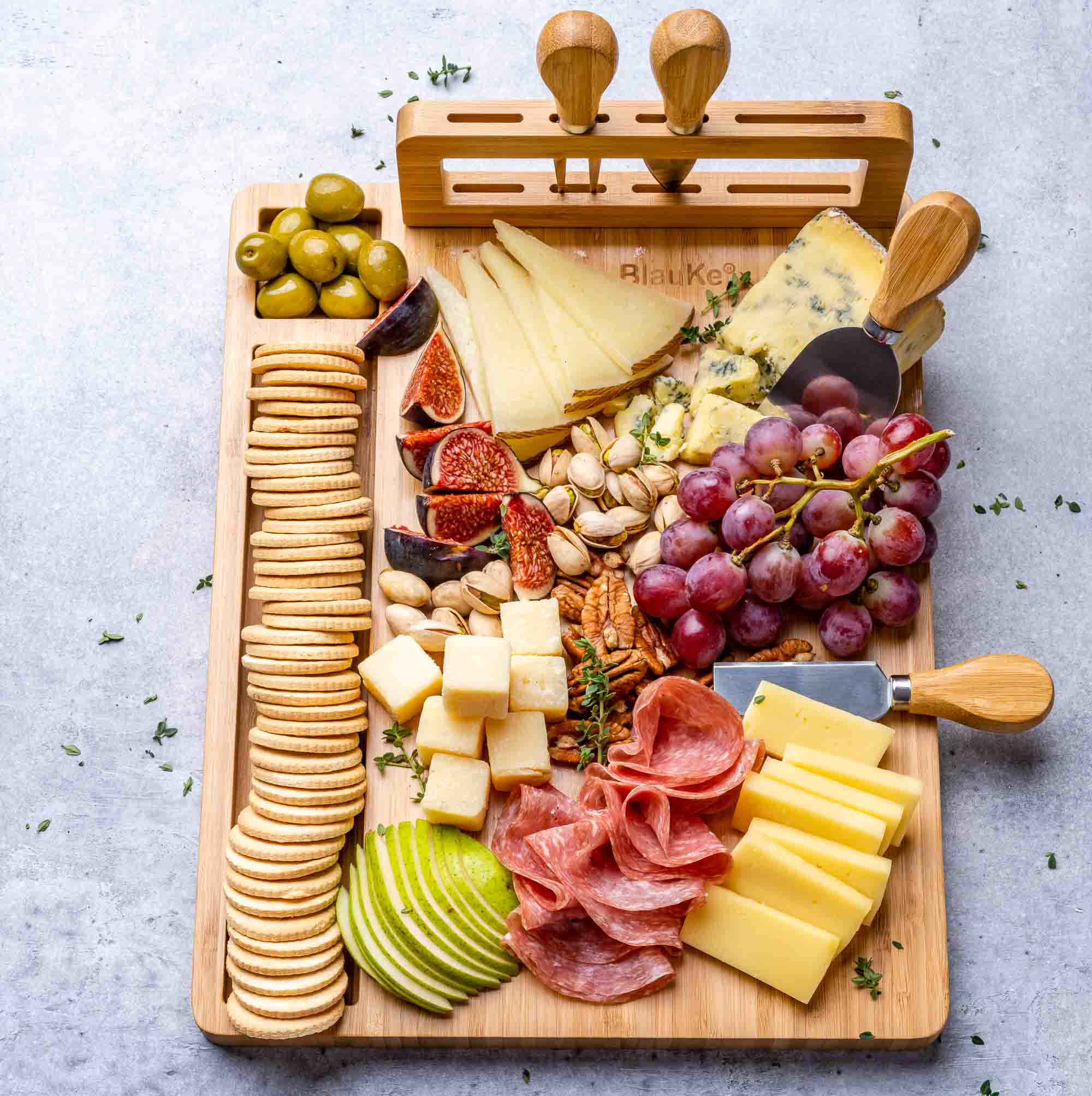 Wooden charcuterie board with assorted meats, cheeses, fruits, and crackers on a light gray background.