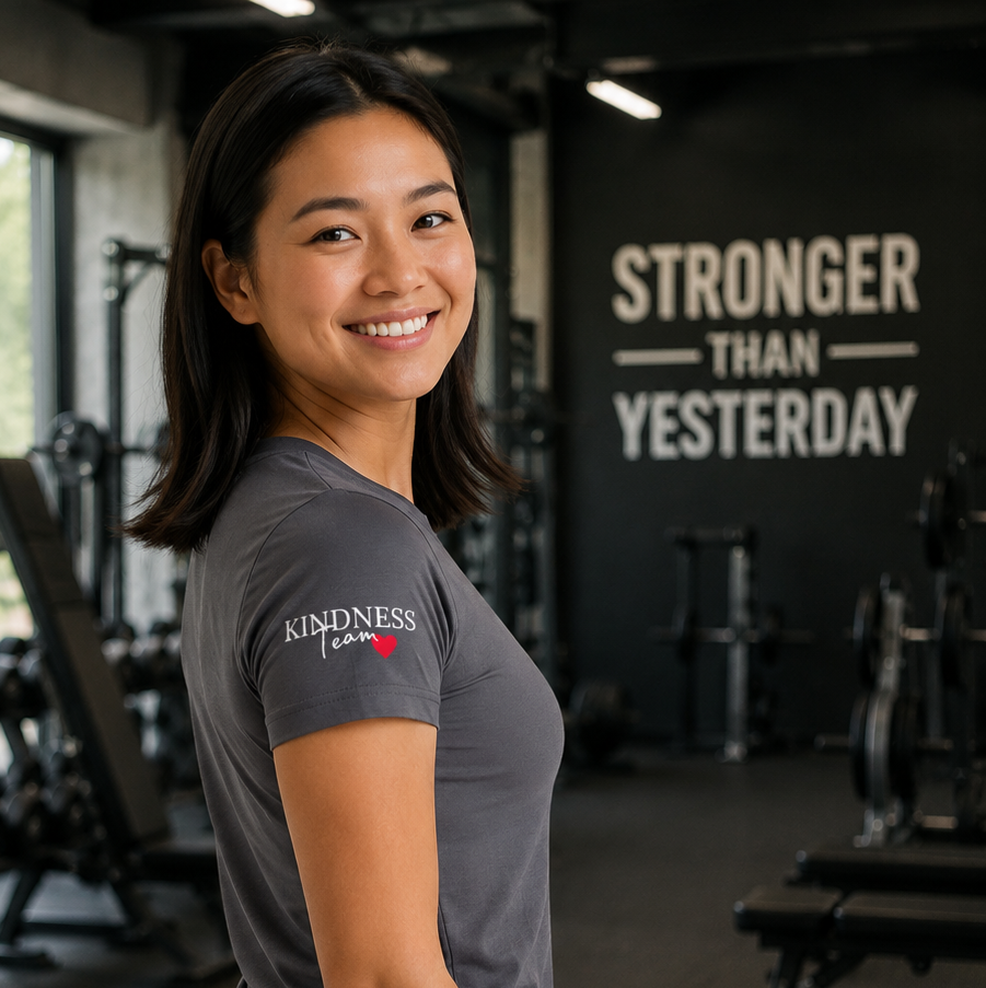 Woman wearing an inspirational message tee for women with 'KINDNESS' logo, in a gym setting with motivational wall art.