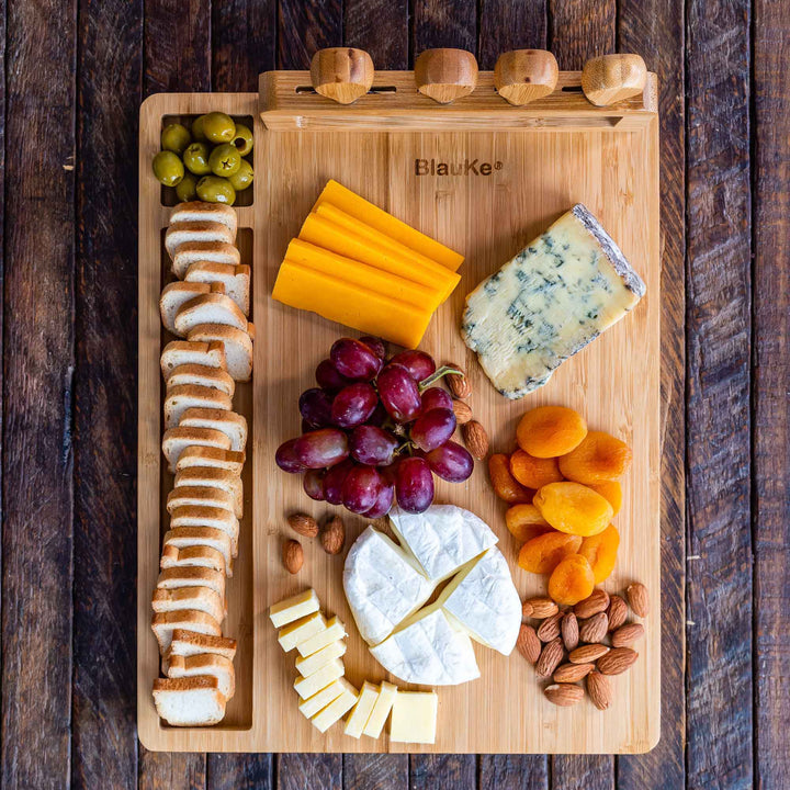 Wooden cutting board with assorted cheeses, fruits, and nuts on a wooden surface