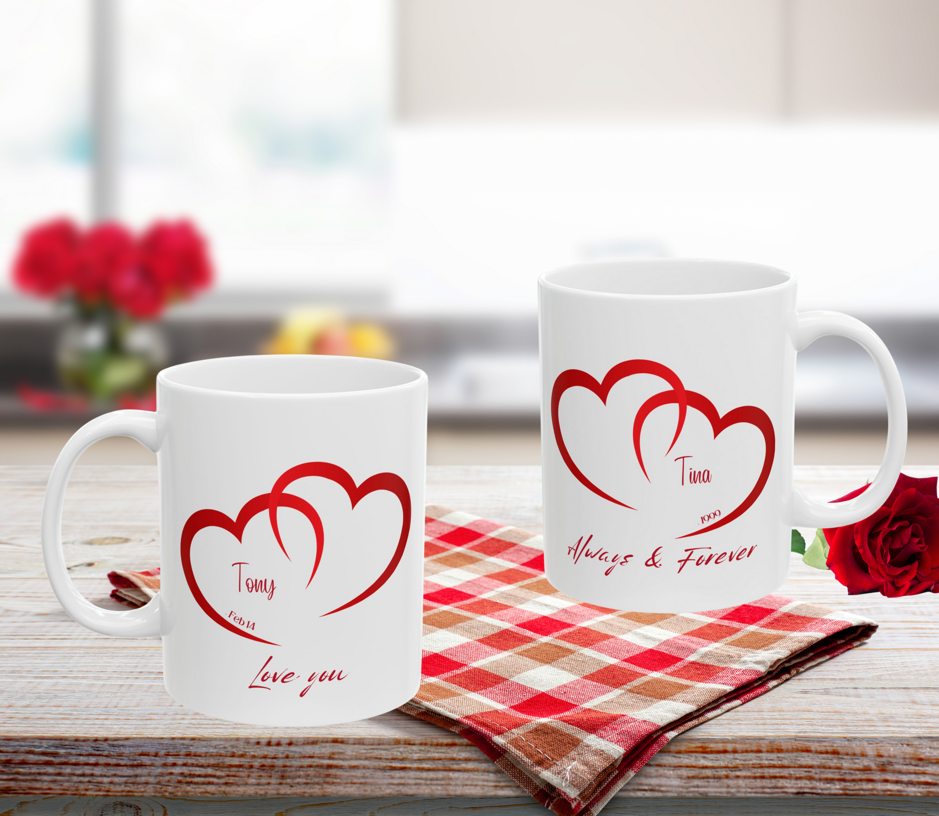 Two white mugs with red heart designs and text on a checkered cloth.