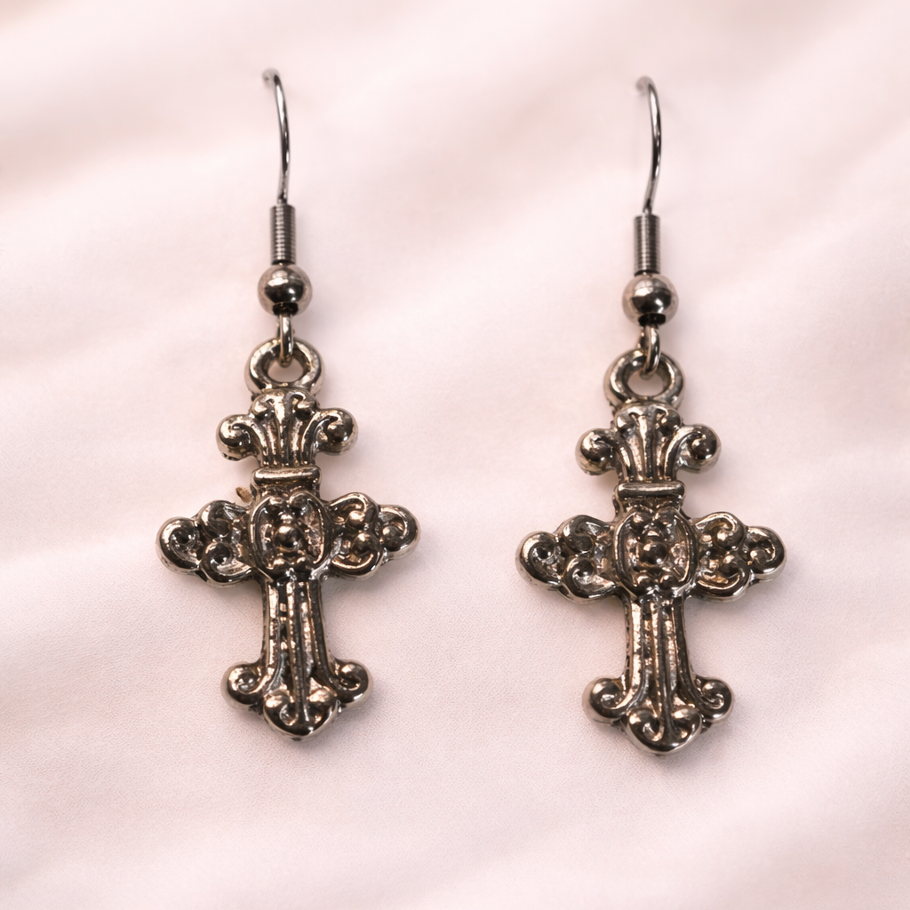 Pair of silver cross earrings on a pink fabric background