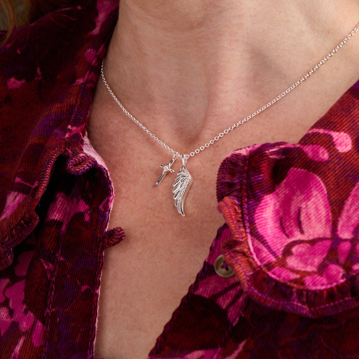Close-up of a woman wearing a silver necklace with a Cross and angel wing pendant. 