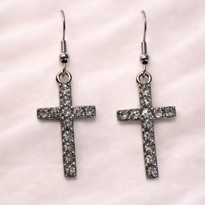 Silver rhinestone cross dangle earrings with hook backs on soft white background