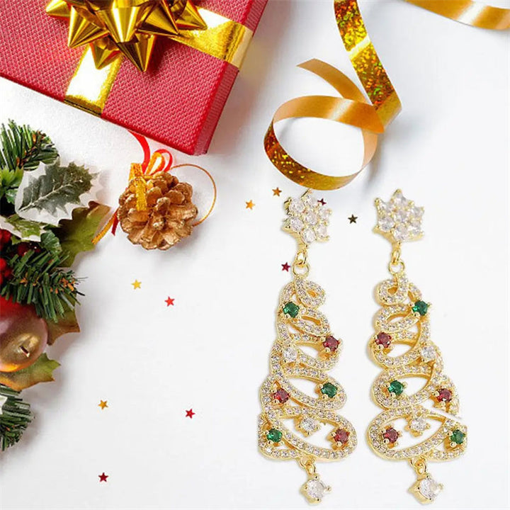 Gold Christmas tree-shaped earrings with gemstones on a white background with festive decorations.