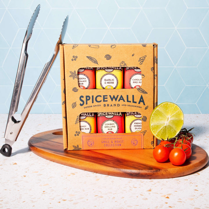 Spicewalla Grill & Roast Collection displayed with tongs, tomatoes, and lime on a wooden cutting board.