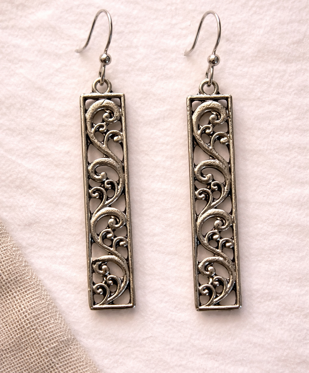 Pair of silver filigree earrings on a textured beige background