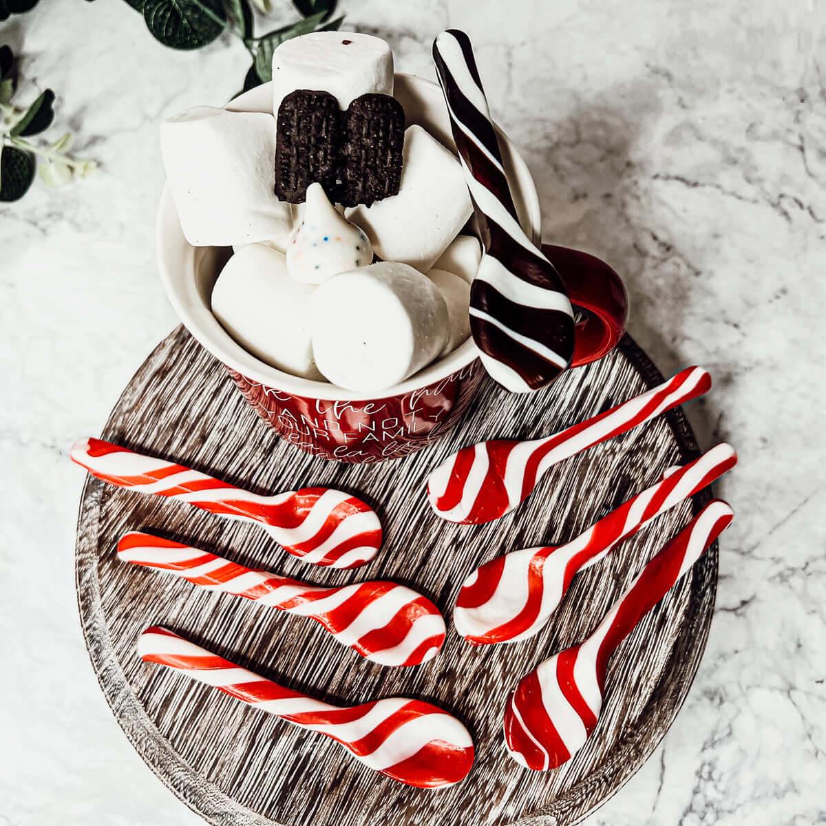 Hot chocolate with marshmallows and candy canes on a wooden board.