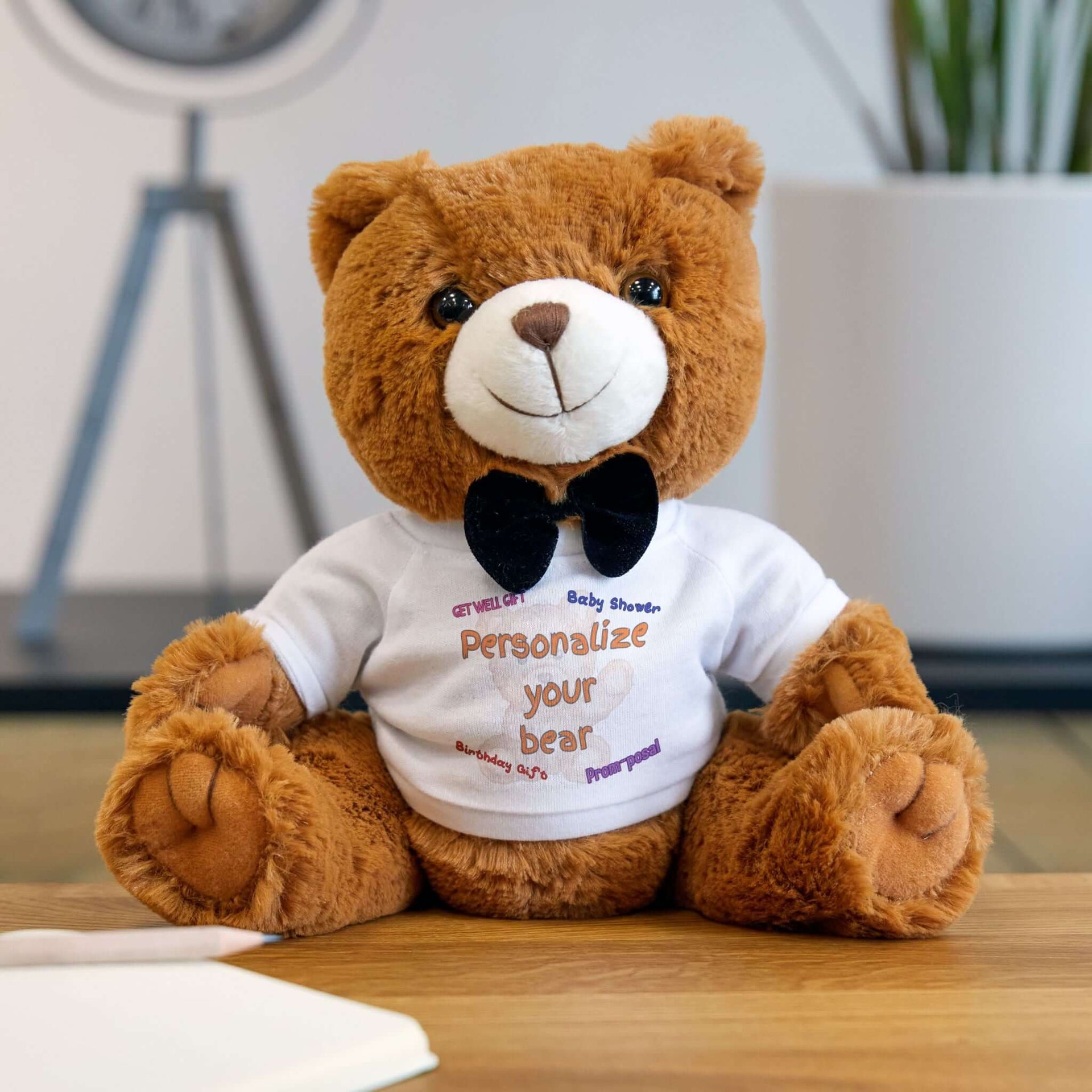 Brown teddy bear wearing a white shirt with a logo on a wooden surface.