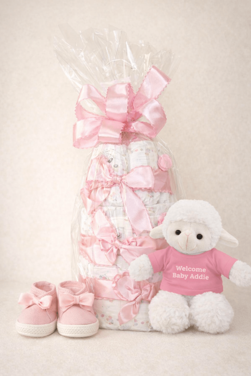 Personalized baby girl diaper cake gift featuring pink details, a plush toy, and adorable baby shoes.