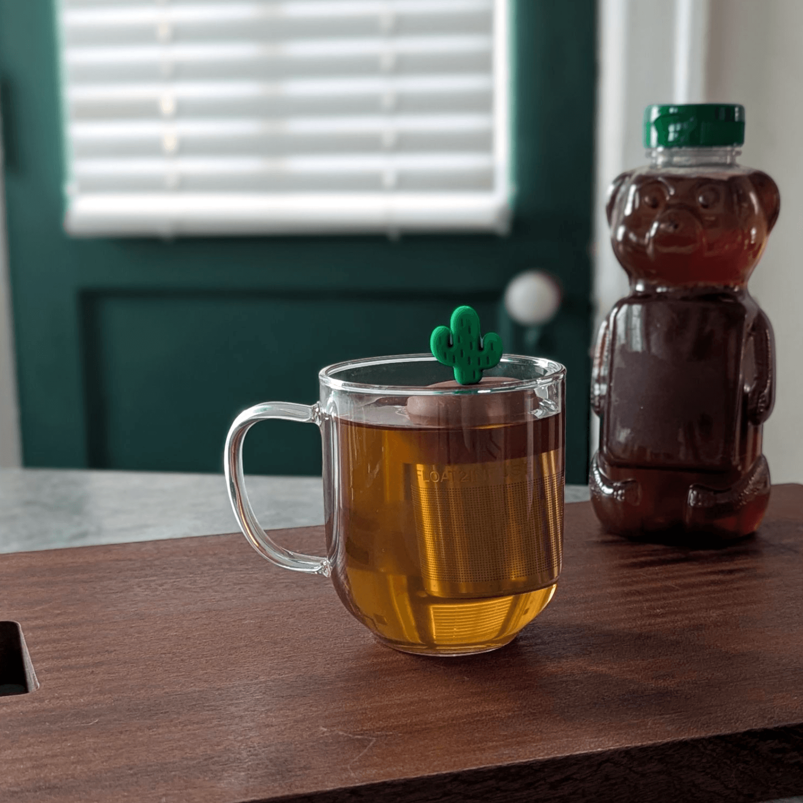 Floating green saguaro cactus tea infuser brewing loose leaf tea in a glass mug with fine mesh stainless steel strainer