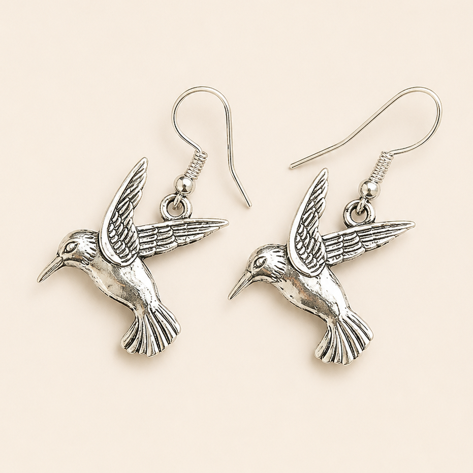Silver hummingbird dangle earrings by Jewelry by Sonya Lee on a soft cream background, lightweight hypoallergenic bird-inspired jewelry.