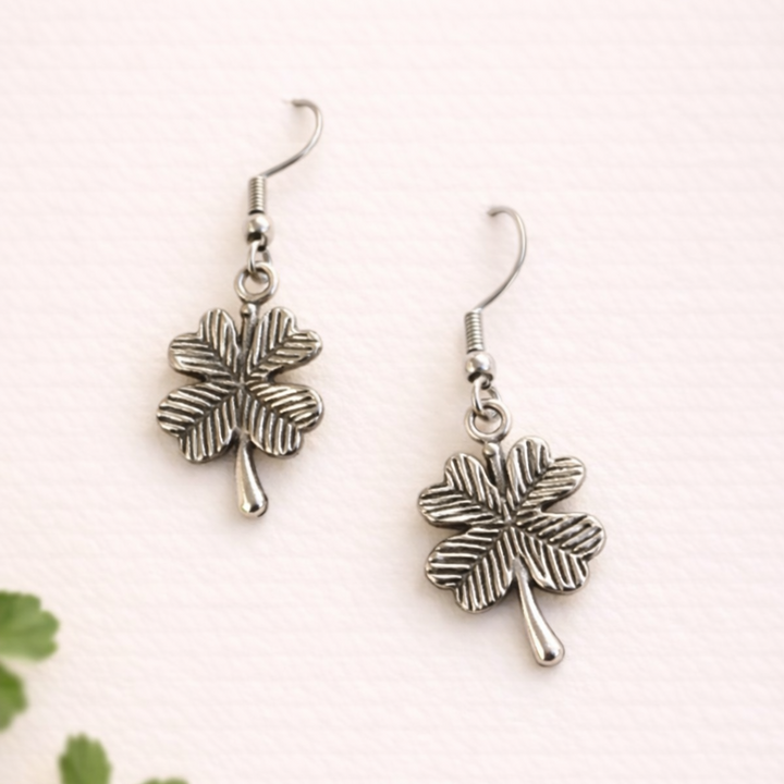 Silver four-leaf clover earrings on a white background with green leaves.