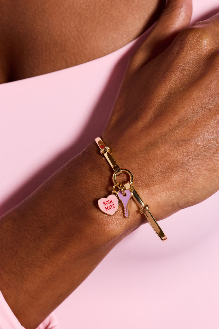 Gold bracelet with charms on a wrist against a pink background