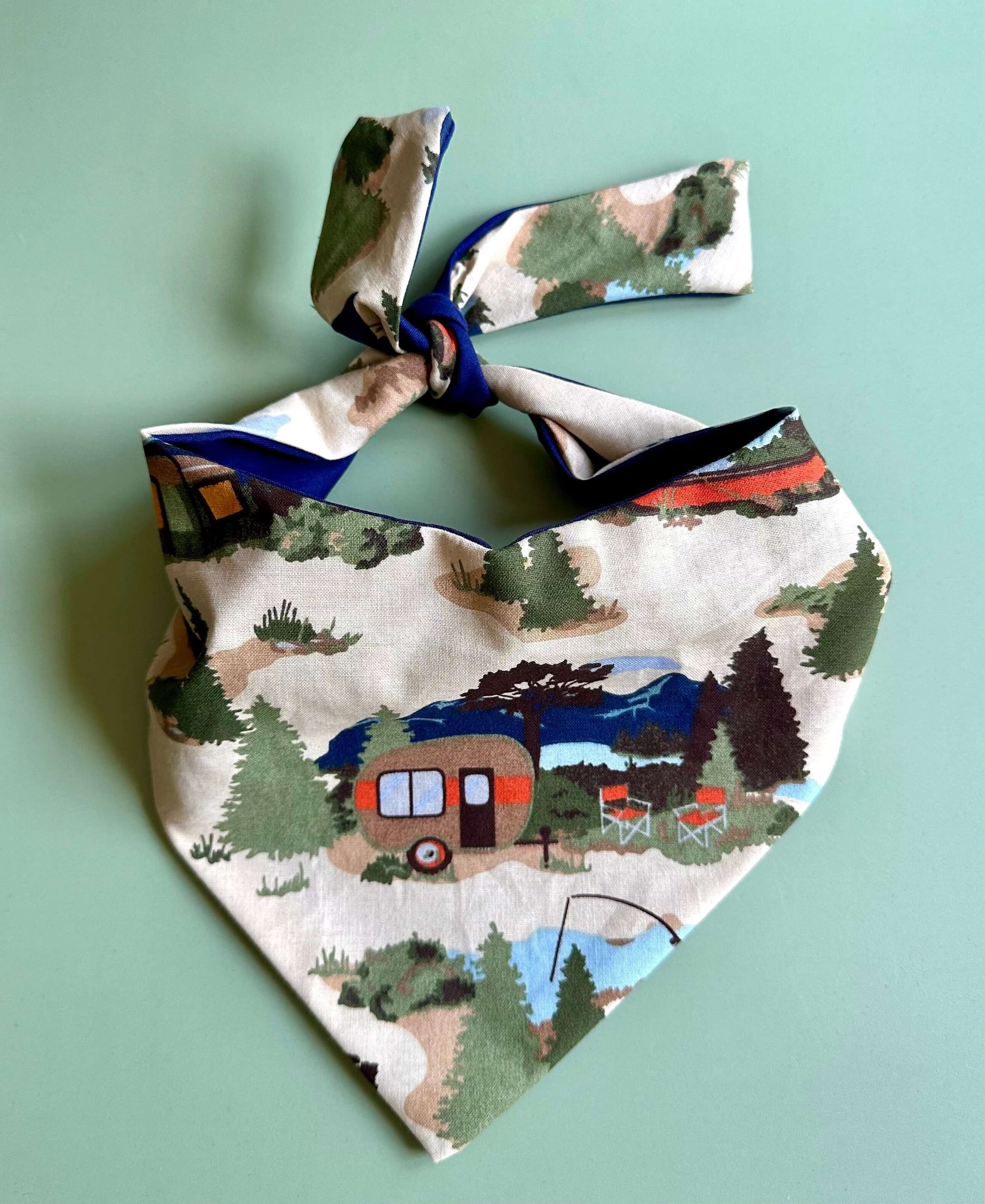 Camping dog bandana with retro camper, lake, mountain, and fishing print displayed flat on mint green background