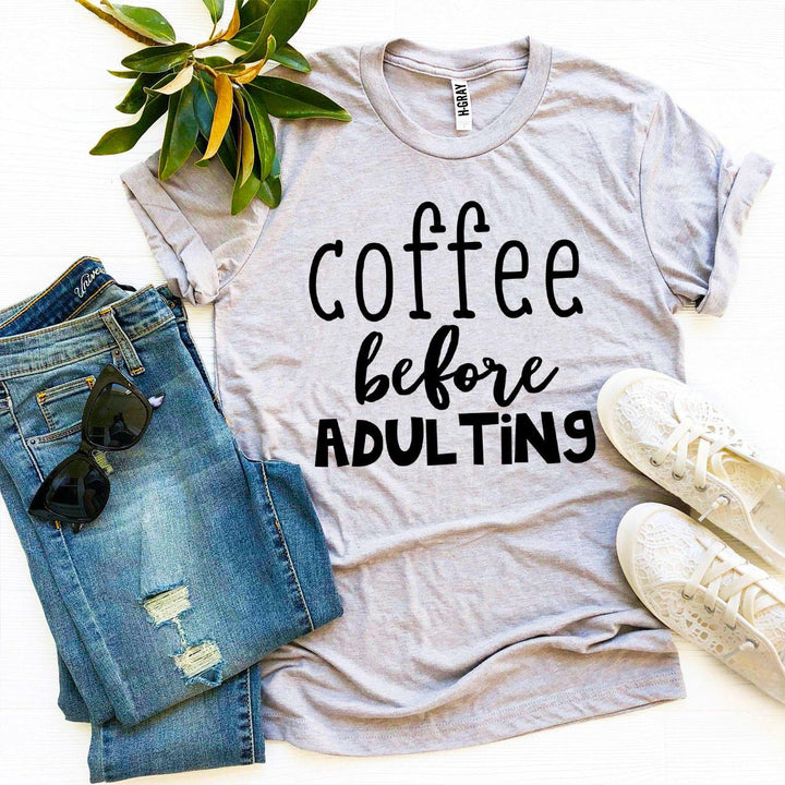 Gray t-shirt with 'Coffee before Adulting' text, paired with jeans and sneakers on a light background