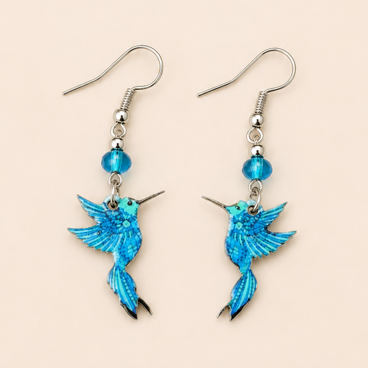Blue hummingbird dangle earrings with turquoise bead accents displayed on a soft cream background.