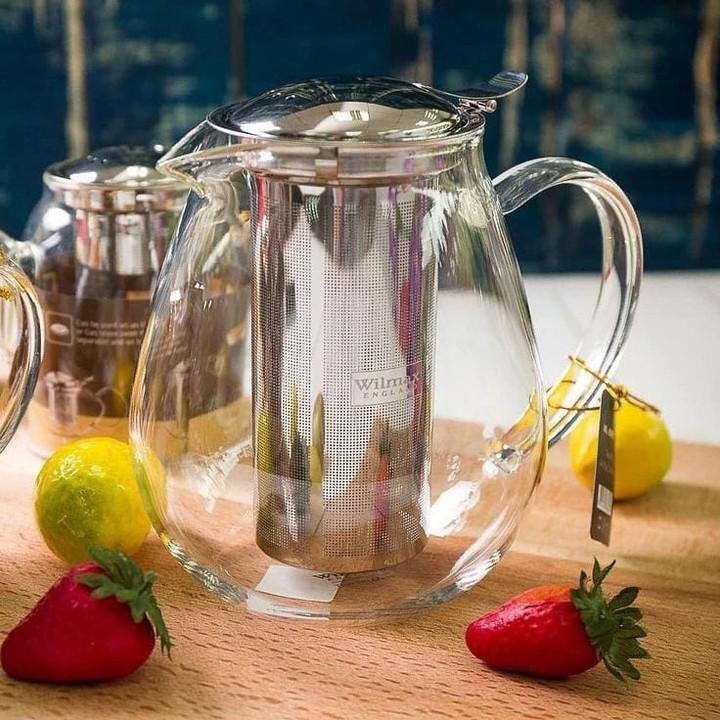 Clear glass teapot with metal infuser on a wooden surface with strawberries and lemons.