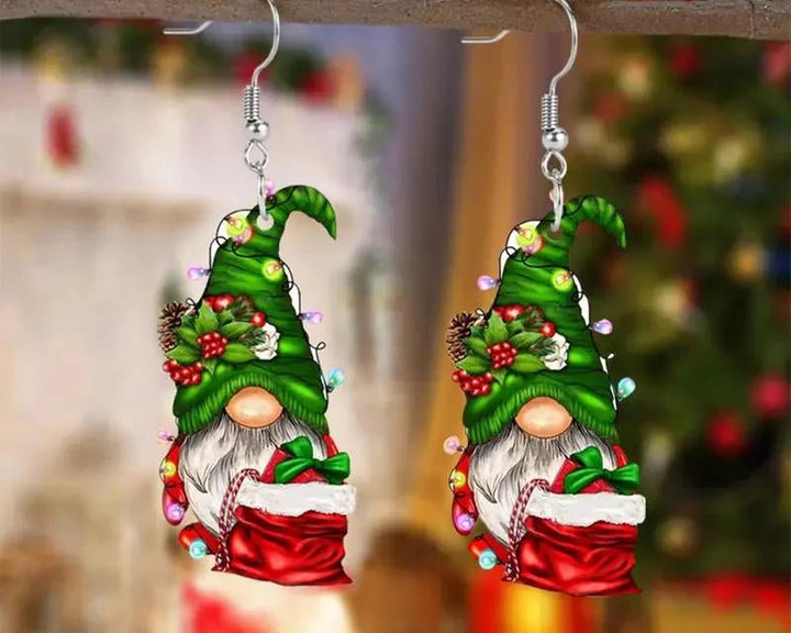 Gnome-shaped earrings with green hats and red outfits against a blurred Christmas tree background.