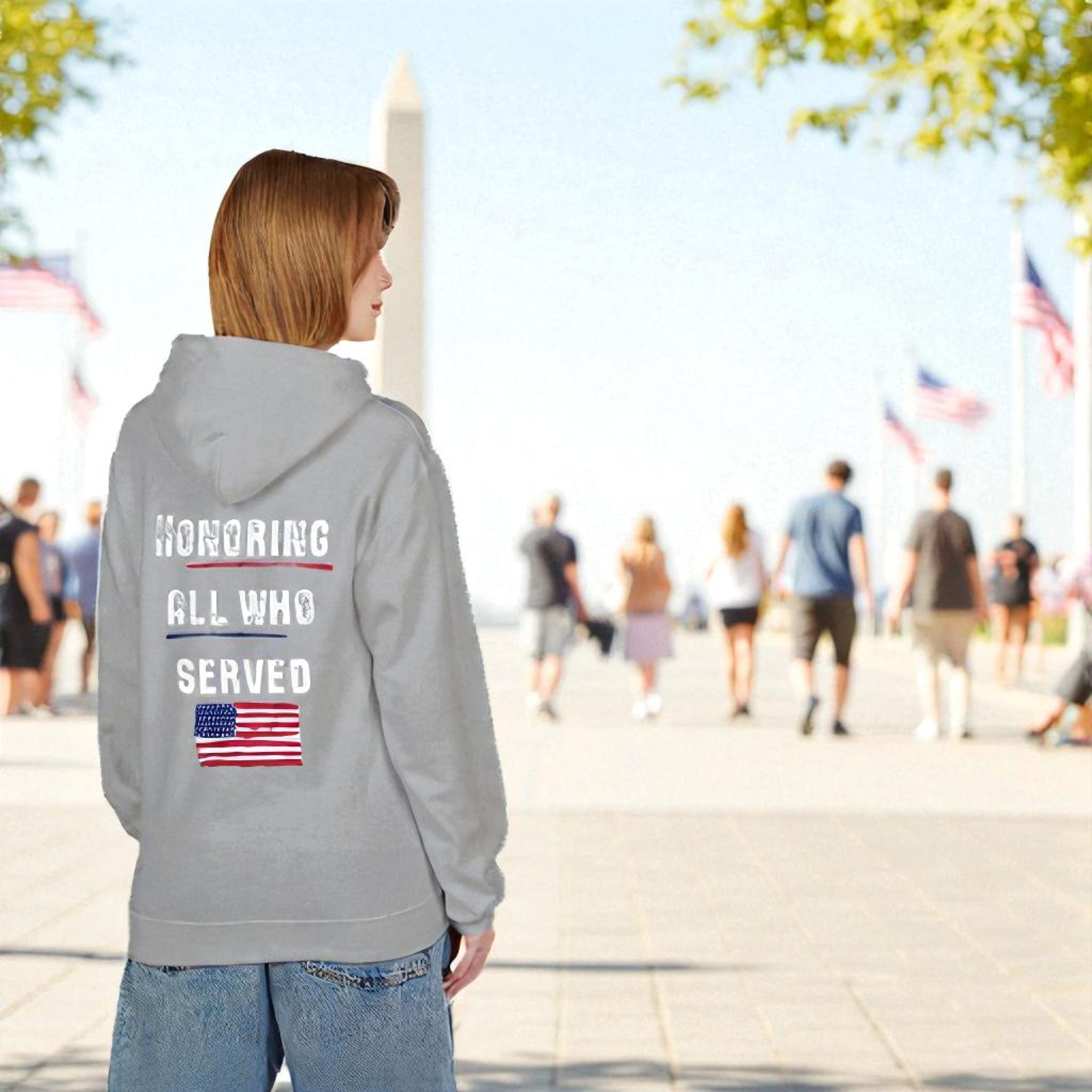 Person wearing a hoodie with 'Honoring All Who Served' text and American flag, standing in front of the Washington Monument.