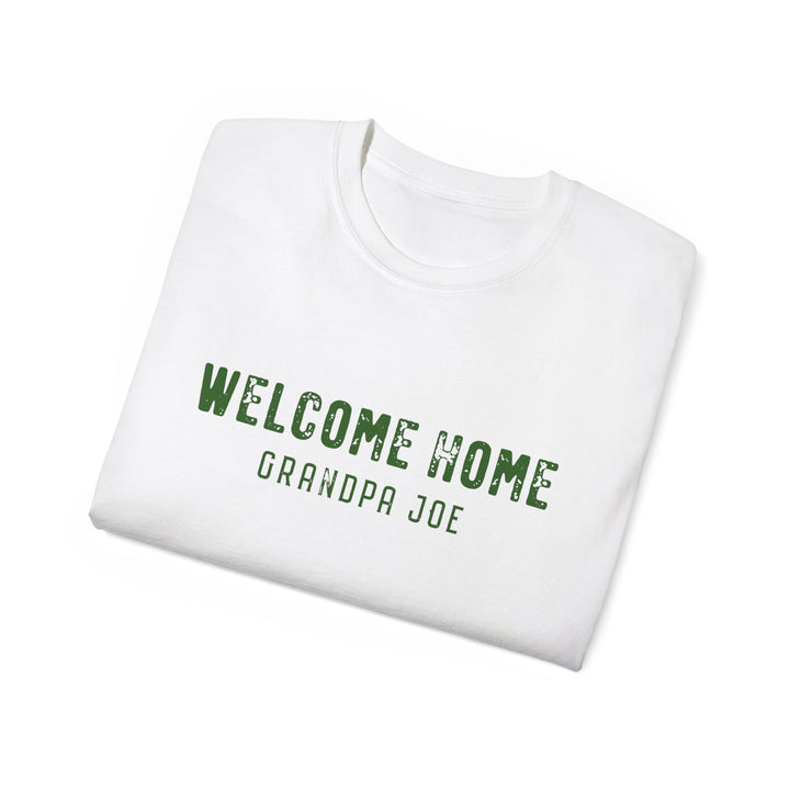 A folded white crewneck t-shirt with 'WELCOME HOME GRANDPA JOE' printed in distressed green text on the front, displayed on a clean white background.
