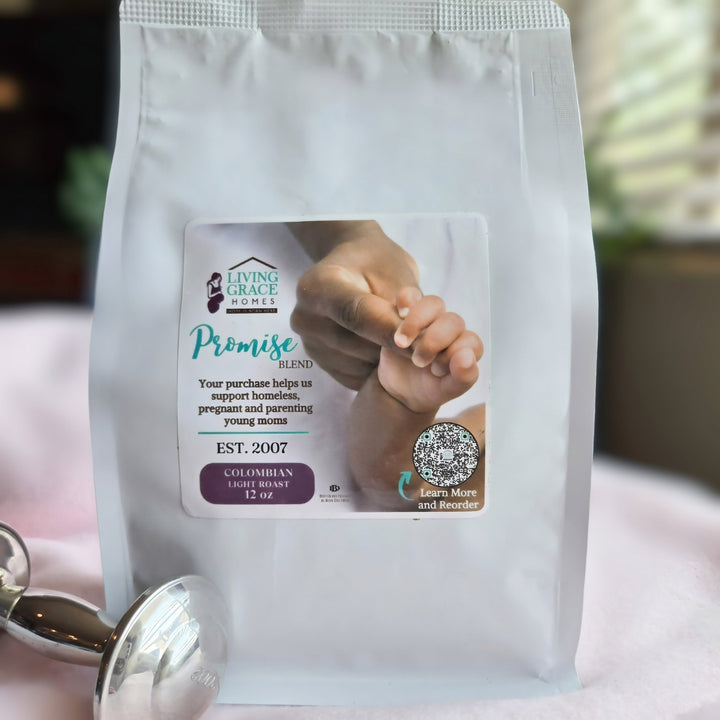 Living Grace Homes Promise Blend coffee bag featuring an image of a mother holding a baby’s hand, placed beside a silver coffee scoop. Colombian light roast 12 oz bag supporting homeless, pregnant, and parenting young moms through nonprofit programs.