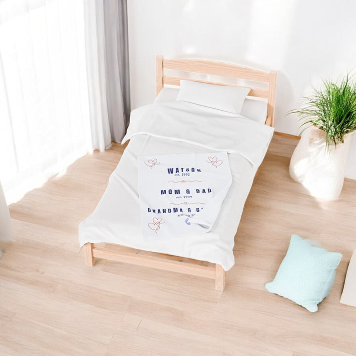 White family timeline blanket with text on a wooden bed in a room with light wood flooring and a plant.