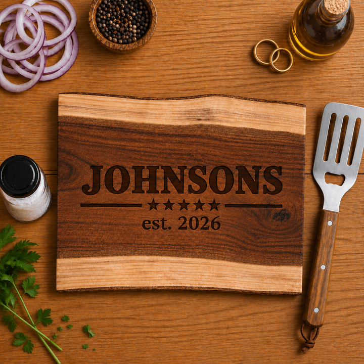 Personalized wood cutting board engraved with “Johnsons” and “est. 2026,” styled with wedding rings as a custom wedding or anniversary gift.